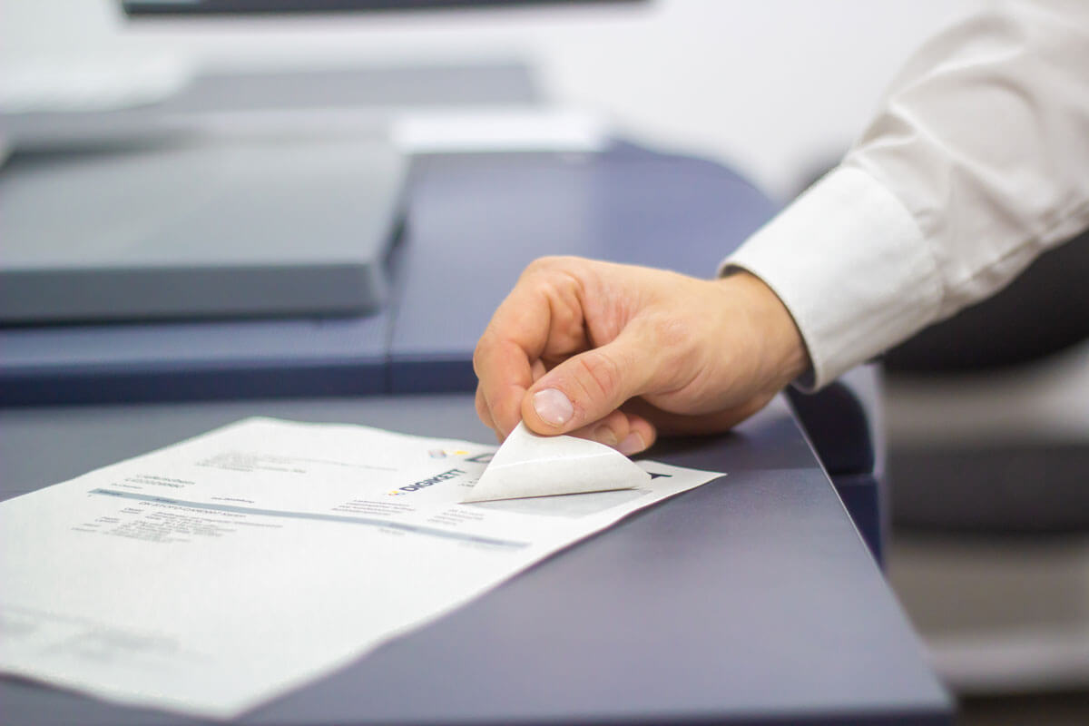 Side view of a printer from which a freshly printed integrated label is being taken by a person.